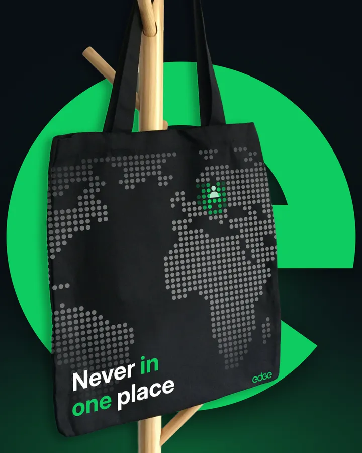 Tote bag negro con la leyenda “Never in one place” sobre fondo verde